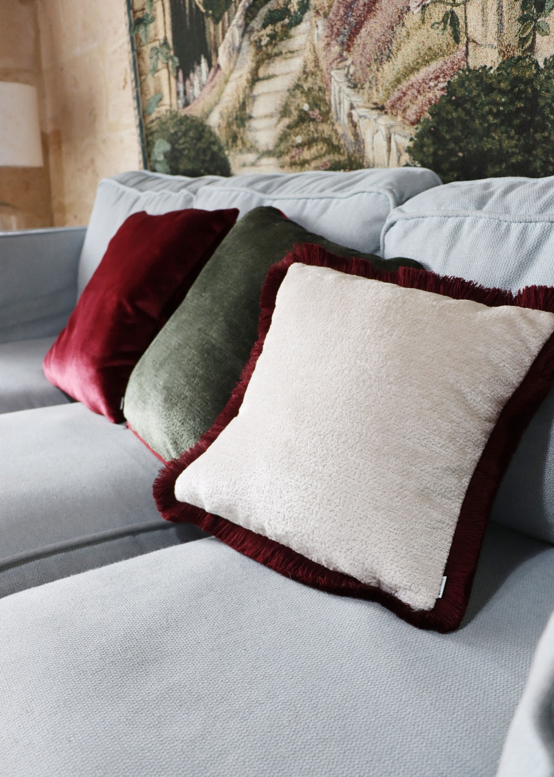 Gray sofa with chenille cushion cover with cotton fringe in a room with decorative elements.