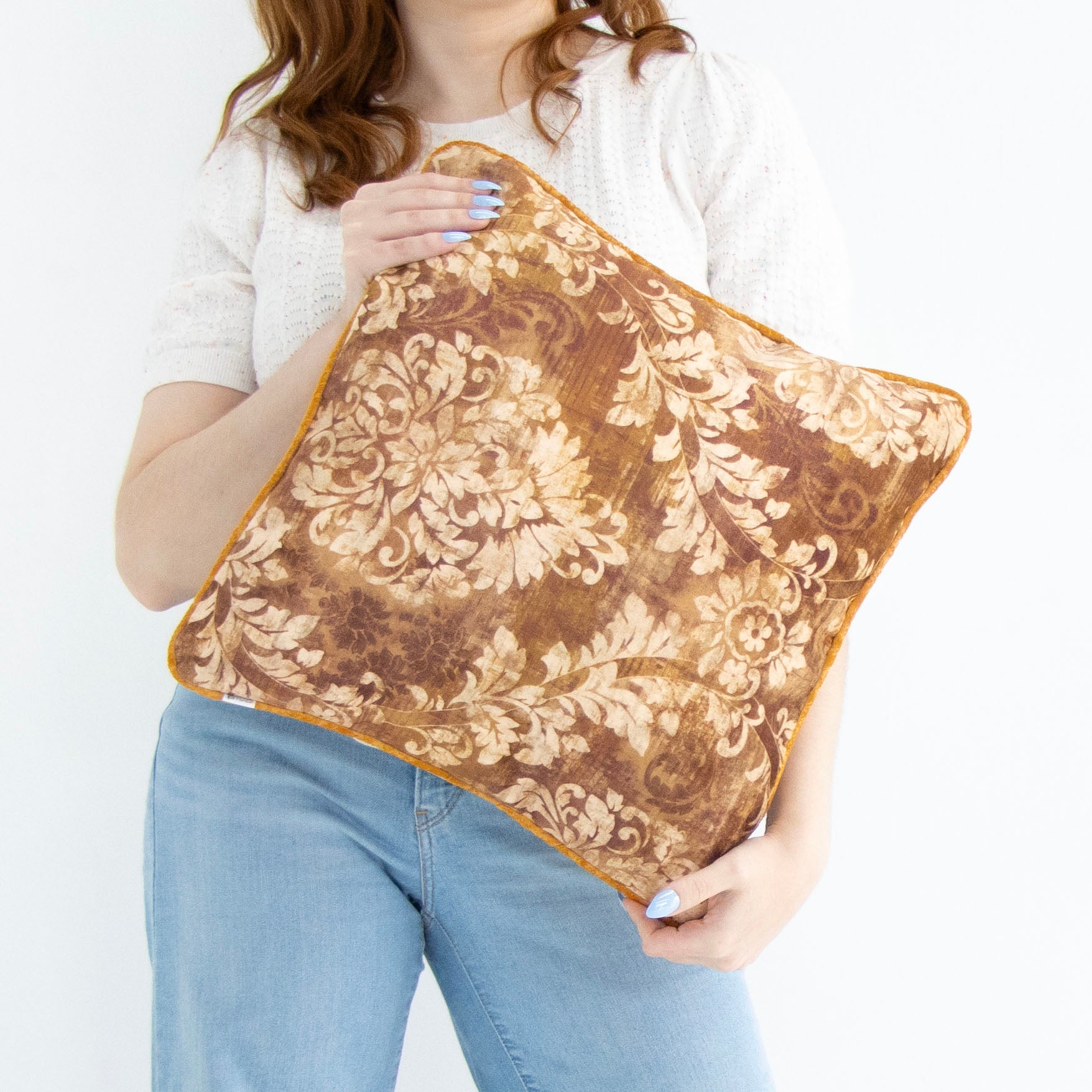 Person holding a brown floral cushion cover with piped edge against a white background