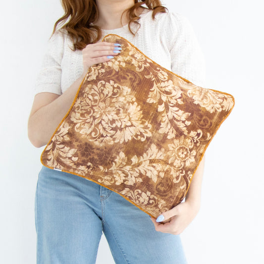 Person holding a brown floral cushion cover with piped edge against a white background