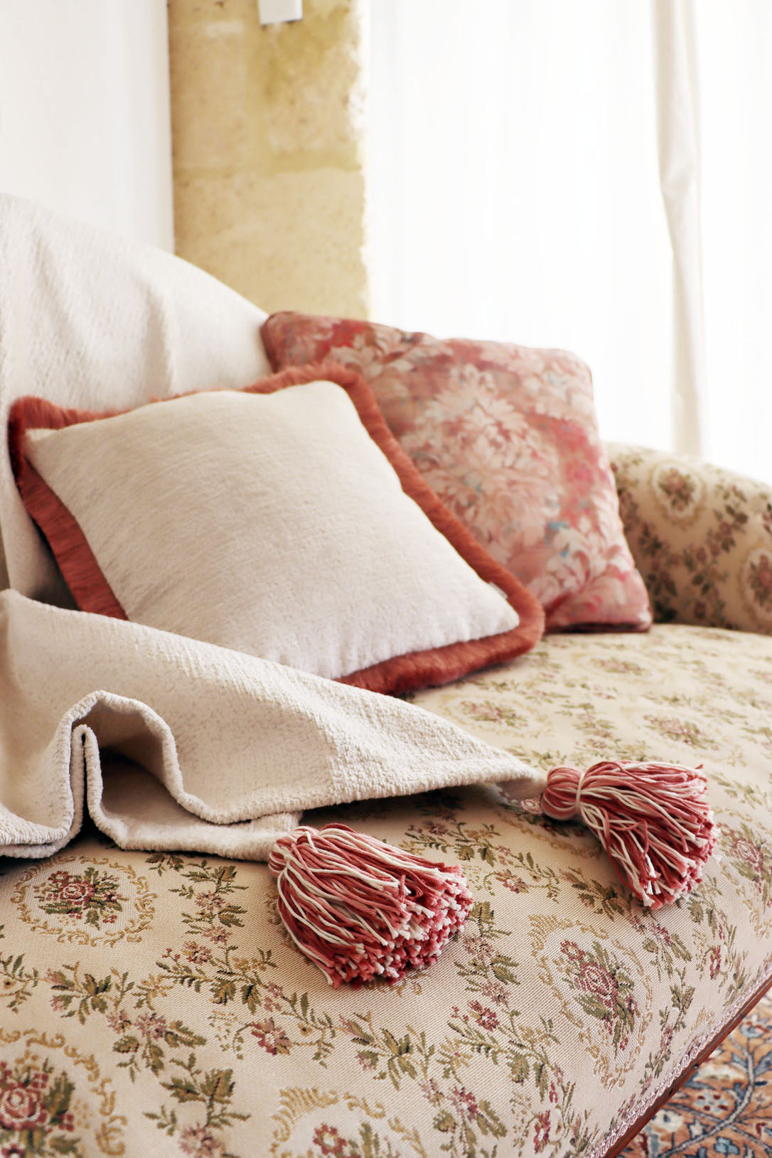 Decorative chenille cushion cover with cotton fringe and blanket on a floral-patterned sofa