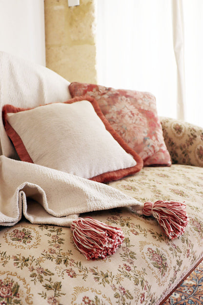 Decorative chenille cushion cover with cotton fringe and blanket on a floral-patterned sofa