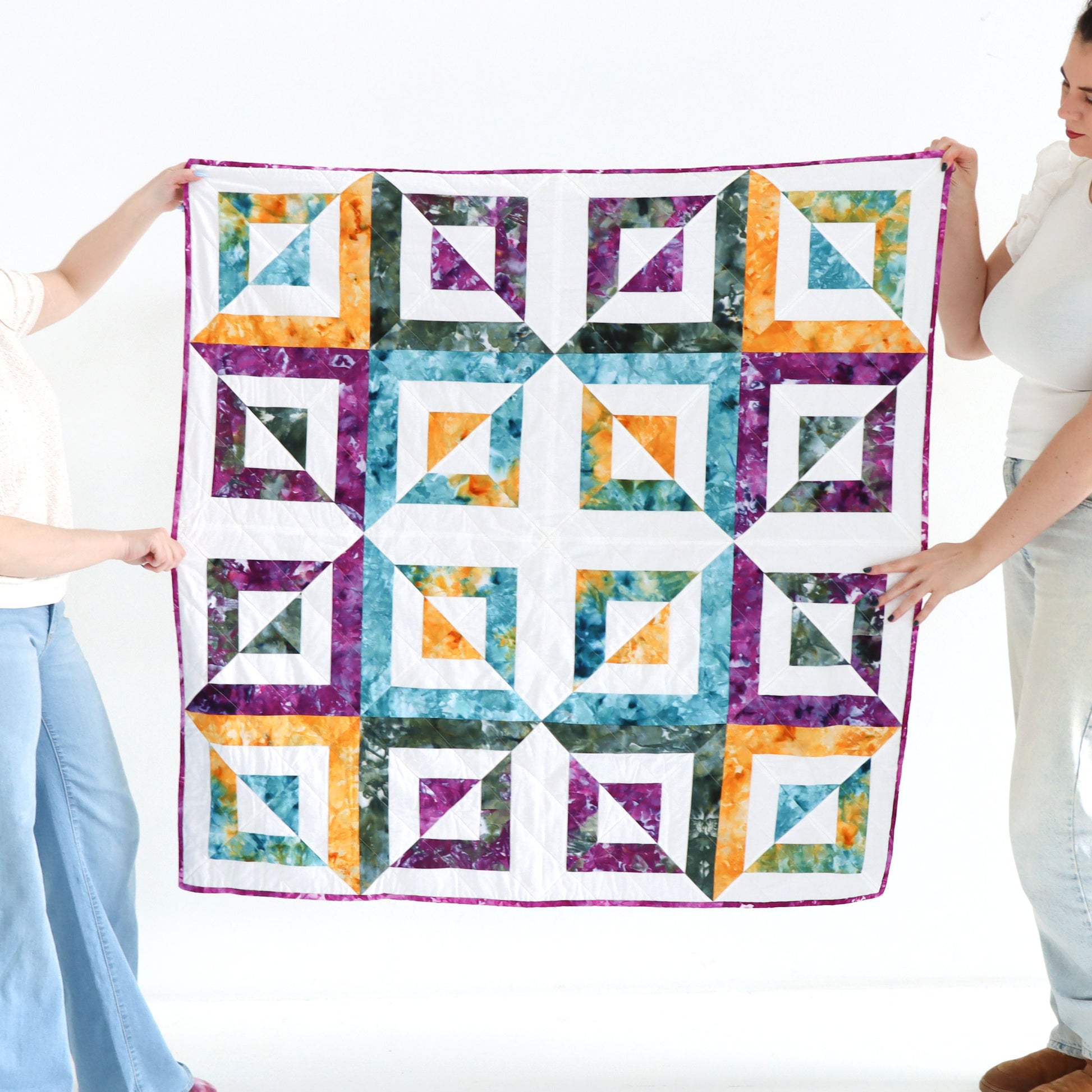 Two people holding a colorful quilt with geometric pattern on a white background