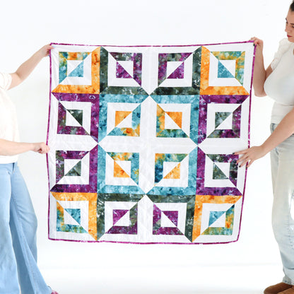 Two people holding a colorful quilt with geometric pattern on a white background
