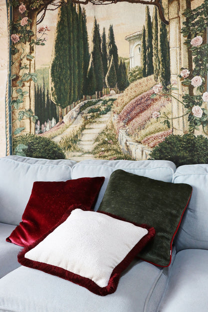 Decorative red chenille cushion cover with cotton fringe on a sofa with a scenic tapestry in the background