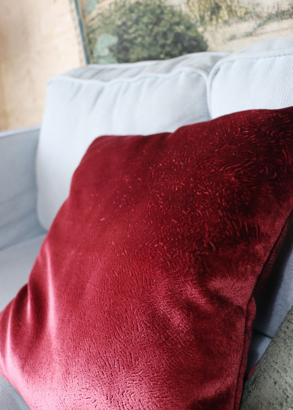 Red textured velvet cushion cover on a light gray sofa with a blurred background
