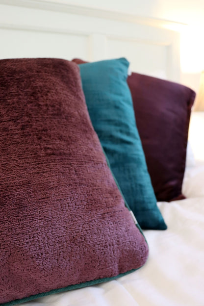 Purple chenille cushion cover with contrasting piping on a bed.