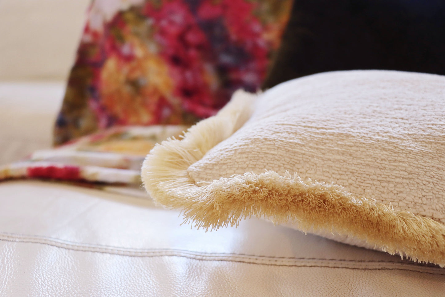 Yellow chenille cushion cover with cotton fringe on a couch with a colourful pillow in the background