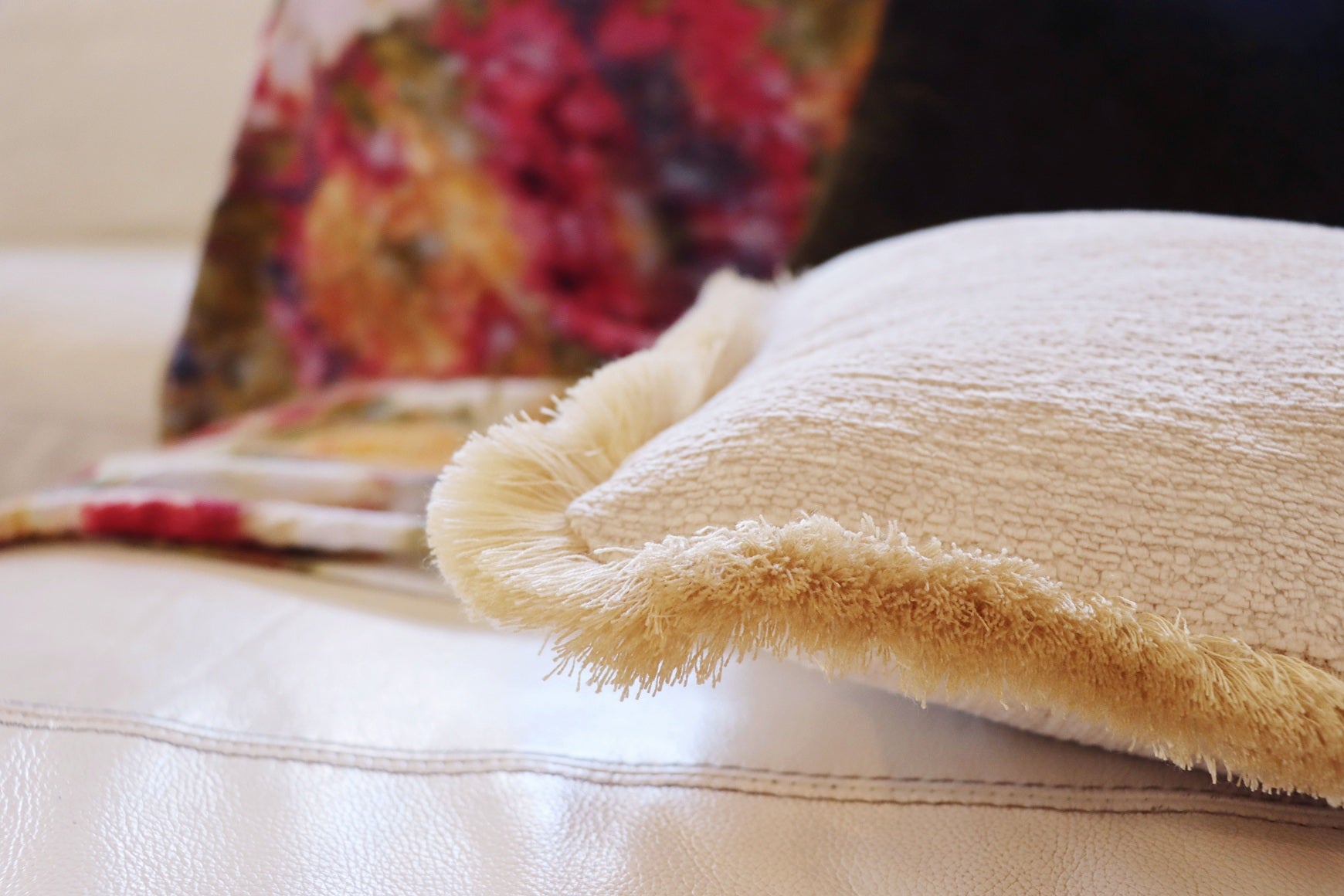 Yellow chenille cushion cover with cotton fringe on a couch with a colourful pillow in the background