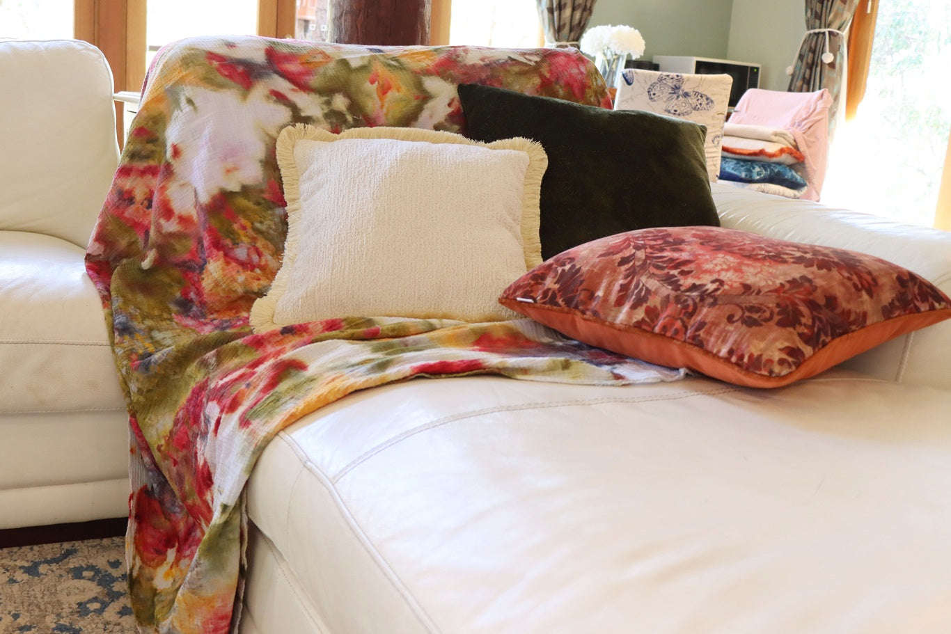 Ice dyed throw draped over a sofa with decorative chenille cushion cover with cotton fringe in a living room setting.