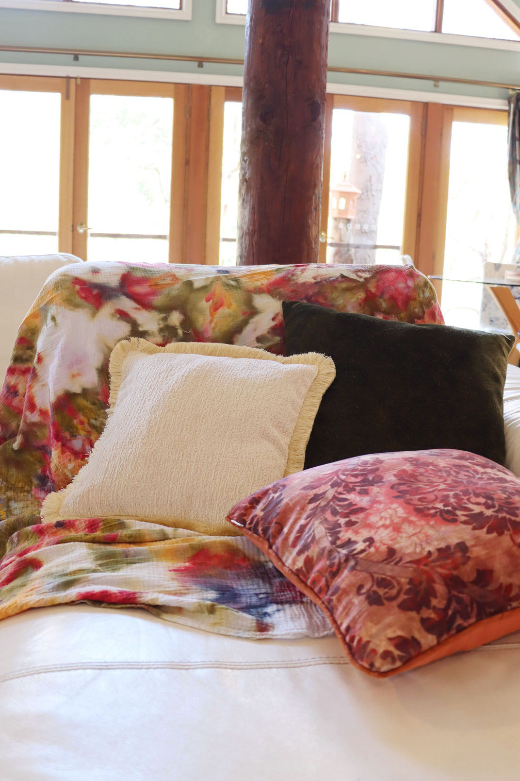 Decorative yellow chenille cushion cover with cotton fringe on a sofa with an ice dyed blanket in a sunlit room.
