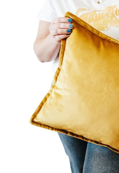 Close up of person holding a mustard yellow velvet cushion cover with flange edging