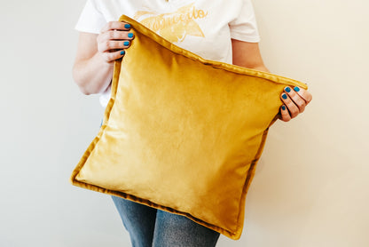 Person holding a mustard yellow velvet cushion cover with flange edging